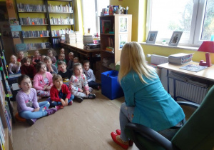 Dzieci siedzą naprzeciwko pani Małgorzaty Hofmann, słuchają ciekawostek na temat książek.